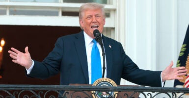 President Donald Trump, arms outstretched speaks from White House balcony.