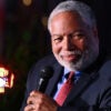 Lonnie Bunch sits while holding a microphone in his left hand as he turns his head to the left.