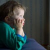 Adorable little boy in green long sleeve shirt, head in hands, stares in rapt attention at an unseen TV.