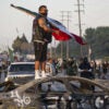 A masked protester stands atop a destroyed car waving a Mexican flag as agitators take over Paramount