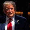 A smiling President Donald Trump partially in shadow.